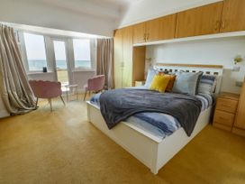 A bedroom with a white bed and pillows a gray blanket two pink chairs by a window with curtains and built in wooden wardrobes at Westbourne in Llandudno