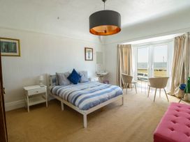 A bedroom with a bed side tables a pink bench two chairs by a window overlooking the sea at Westbourne in Llandudno