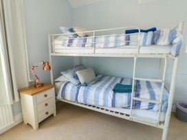 A bedroom with a white bunk bed with blue striped bedding next to a white nightstand with a copper desk lamp at Westbourne in Llandudno