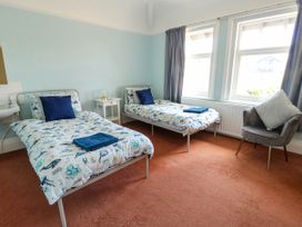 A bedroom with two single beds a white side table a gray chair and three windows at Westbourne in Llandudno