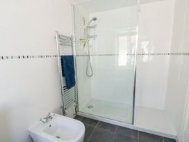 A bathroom with a bidet a glass shower enclosure a chrome towel radiator with a blue towel and white tiled walls at Westbourne in Llandudno