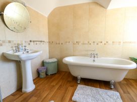 A bathroom with a pedestal sink a round mirror a clawfoot bathtub a laundry basket and a small trash bin at Westbourne in Llandudno