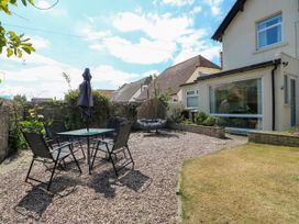 An outdoor patio with a table and chairs an umbrella and a hanging chair next to a house at Westbourne in Llandudno