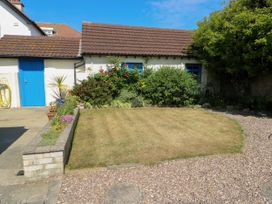 A small garden with grass and bushes in front of a white house with a brown tiled roof and blue door and windows at Westbourne in Llandudno