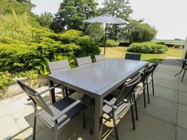 A garden with a table and chairs under an umbrella at Clynnog House in Dwyran near Newborough