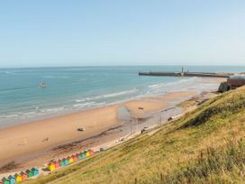 A beach with colorful huts and a pier at Sail Away, 17 Union Mill in Whitby