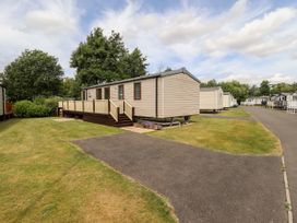 A row of mobile homes on grass with paved driveway and trees in the background at 19 The Brambles in Humberston Lincolnshire