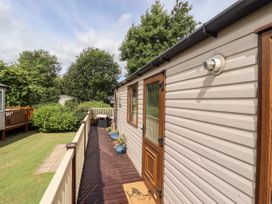 An exterior view of a mobile home with a wooden deck and railing surrounded by grass and trees at 19 The Brambles in Humberston Lincolnshire