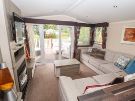 A living room with a sectional sofa coffee table wall-mounted TV and glass doors leading to a deck at 19 The Brambles in Humberston Lincolnshire