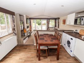 An open-plan kitchen dining and living area with a wooden dining table and chairs a washing machine microwave and sofa with windows and blinds at 19 The Brambles in Humberston Lincolnshire