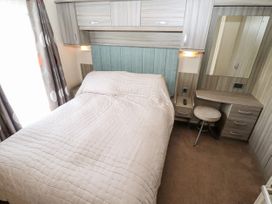 A bedroom with a bed covered by a quilt next to a desk with a stool and a mirror at 19 The Brambles in Humberston Lincolnshire