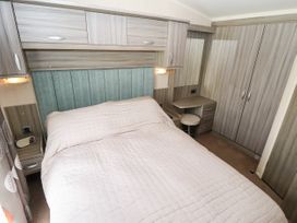 A bedroom with a bed covered with a quilted cover and built in wooden cabinets with a dressing table and stool at 19 The Brambles in Humberston Lincolnshire