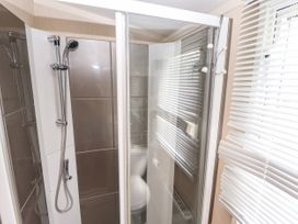 A shower area with a handheld shower head and a glass door next to a window with blinds at 19 The Brambles in Humberston Lincolnshire