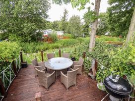 An outdoor deck with a round table and six chairs surrounded by greenery and trees at 19 The Brambles in Humberston Lincolnshire
