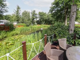 An outdoor deck with wicker chairs and a round table next to a pond with water plants and surrounded by trees and greenery at 19 The Brambles in Humberston Lincolnshire