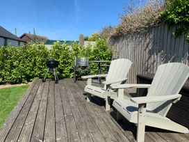 A patio with wooden decking, chairs and grill at Lavender Barn Crantock