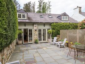 A stone patio with outdoor chairs and tables outside a cottage with dormer windows at Garden Cottage in Garndolbenmaen near Tremadog