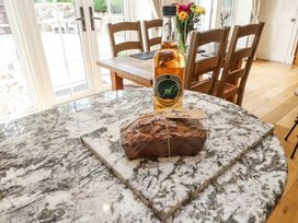 A kitchen with a marble countertop a loaf of bread wrapped in plastic and a bottle on the counter and a wooden dining table with chairs and flowers at Garden Cottage in Garndolbenmaen near Tremadog