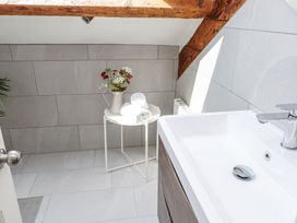 A bathroom with a white sink a small round table with rolled towels and a vase with flowers at Garden Cottage in Garndolbenmaen near Tremadog