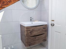 A bathroom sink with wooden cabinet and a round mirror on a tiled wall at Garden Cottage Garndolbenmaen near Tremadog