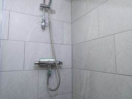 A shower area with a wall-mounted showerhead and control unit in a tiled bathroom at Garden Cottage Garndolbenmaen near Tremadog