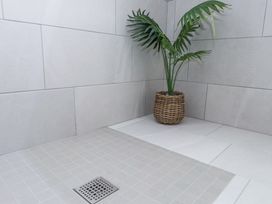A corner of a tiled bathroom with a floor drain and a potted plant in a wicker basket