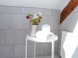 A small white round table with a pitcher of flowers and two rolled white towels in a tiled room at Garden Cottage in Garndolbenmaen near Tremadog