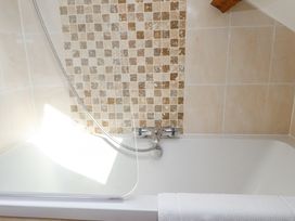 A bathtub with a shower attachment and tiled walls with beige and brown square patterns at Garden Cottage in Garndolbenmaen near Tremadog