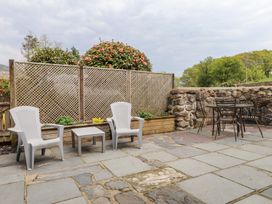 An outdoor patio with two white plastic chairs and a small table next to a wooden lattice fence and a round metal table with four chairs near a stone wall at Garden Cottage in Garndolbenmaen near Tremadog