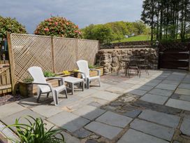 A stone patio with two white plastic chairs and a table and a round metal table with chairs at Garden Cottage in Garndolbenmaen near Tremadog