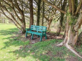 A green bench under trees on a grassy area at Garden Cottage in Garndolbenmaen near Tremadog