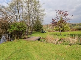 A grassy outdoor area with trees a small wooden bridge and a picnic table at Garden Cottage in Garndolbenmaen near Tremadog