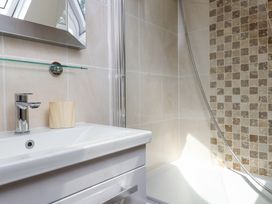 A bathroom sink with a faucet and a wooden cup next to a bathtub with tiled walls at Garden Cottage in Garndolbenmaen near Tremadog