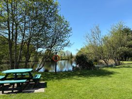 A picnic table near a pond surrounded by trees with a lifebuoy on a post at Garden Cottage in Garndolbenmaen near Tremadog