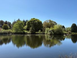 A pond with trees and bushes on the bank under a clear sky at Garden Cottage in Garndolbenmaen near Tremadog