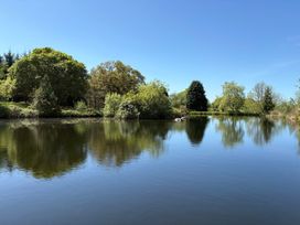 A pond surrounded by various trees and bushes under a clear blue sky at Garden Cottage in Garndolbenmaen near Tremadog