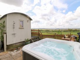 An outdoor hot tub near a small shed with an outdoor shower and a wooden table with chairs at Shepherds Hut Colton near Rugeley Staffordshire