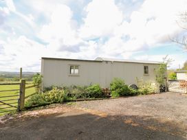 An exterior view of a corrugated metal building with two windows surrounded by plants and a gravel driveway at Shepherds Hut in Colton near Rugeley Staffordshire