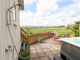 An outdoor patio with a shower hot tub small table and chairs and a wooden fence overlooking fields at Shepherds Hut in Colton near Rugeley Staffordshire