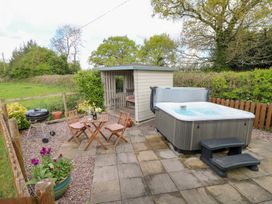 An outdoor patio with a hot tub, wooden table and chairs, a barbecue grill, and a small shed at Shepherds Hut Colton near Rugeley Staffordshire