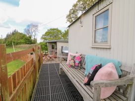 An outdoor seating area with a wooden bench and cushions next to a small fenced yard at Shepherds Hut in Colton near Rugeley Staffordshire