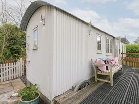 An exterior view of a corrugated metal shepherds hut with a wooden bench and cushions on the deck at Shepherds Hut in Colton near Rugeley Staffordshire
