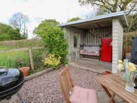 A garden seating area with a wooden table and chair a small shelter with a bench and a red refrigerator at Shepherds Hut in Colton near Rugeley Staffordshire