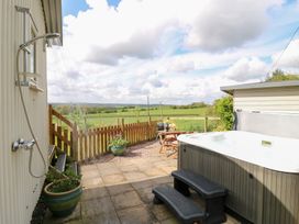 An outdoor patio with a hot tub small table with chairs and an outdoor shower overlooking a green field at Shepherds Hut Colton near Rugeley Staffordshire
