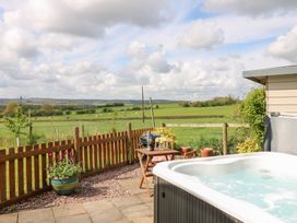 An outdoor patio area with a hot tub wooden table and chairs a potted plant and a fenced grassy field with cows at Shepherds Hut in Colton near Rugeley Staffordshire