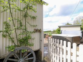 An outdoor area with a white picket gate labeled shepherds hut a hot tub wooden shed and a plant growing on a cart wheel at Shepherds Hut in Colton near Rugeley Staffordshire