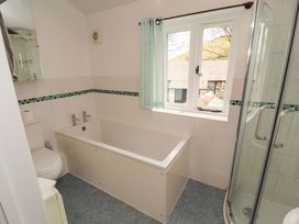 A bathroom with a bathtub, shower, toilet, and a window at One Town End in Mungrisdale, Mosedale