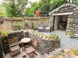 A garden with a stone wall, table, chairs, and a shed at Fellside Cottage in Bowness-On-Windermere