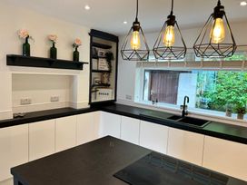 A kitchen with black countertops white cabinets hanging lights and a window with plants at Afallon Menai Bridge