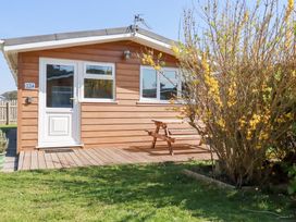 A wooden cabin with white door and windows a picnic table on a deck and a flowering bush in the yard at 224 Atlantic Bays in St Merryn